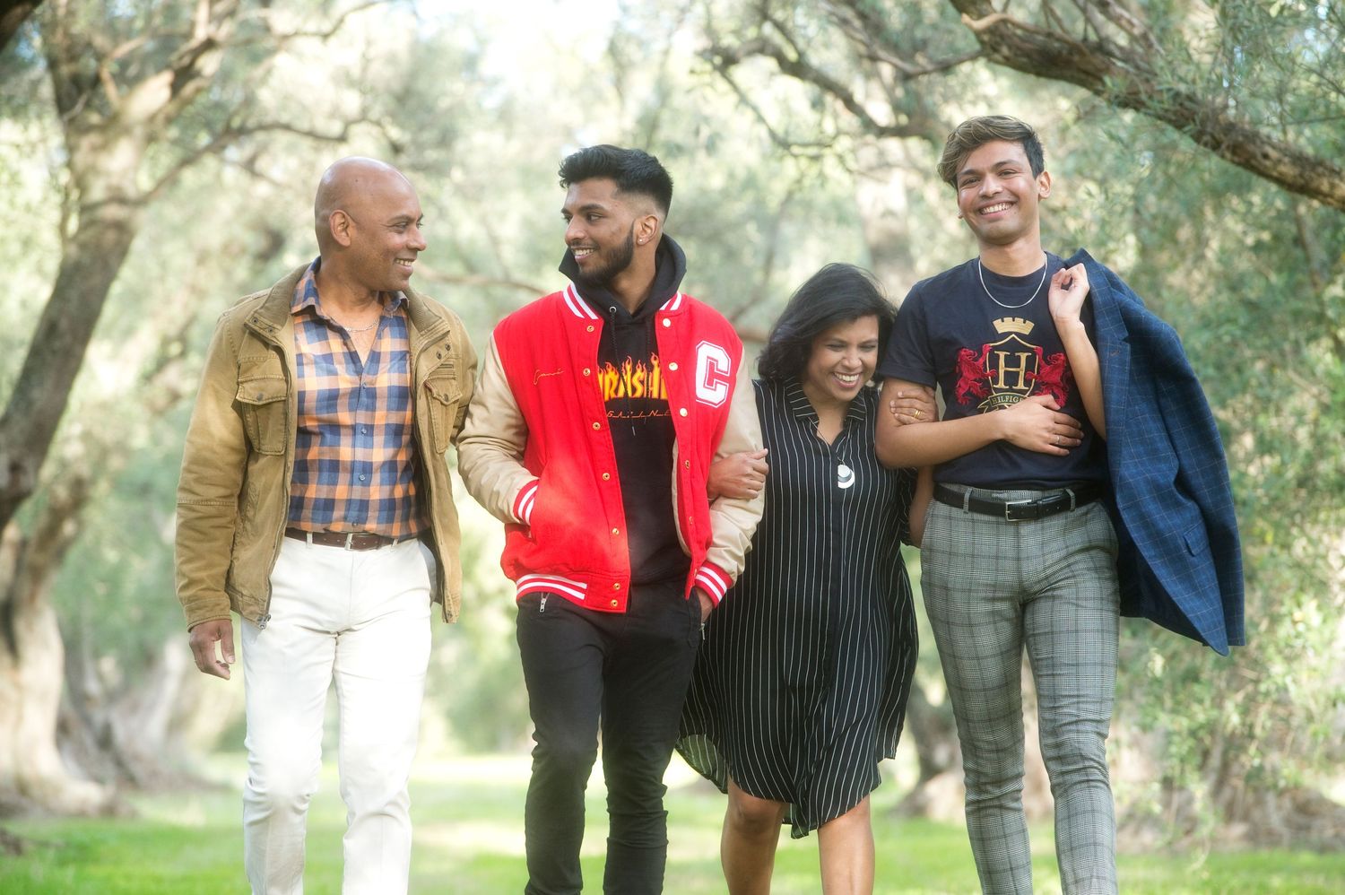 Candid outdoor portrait of four family members walking and laughing together in a wooded setting.