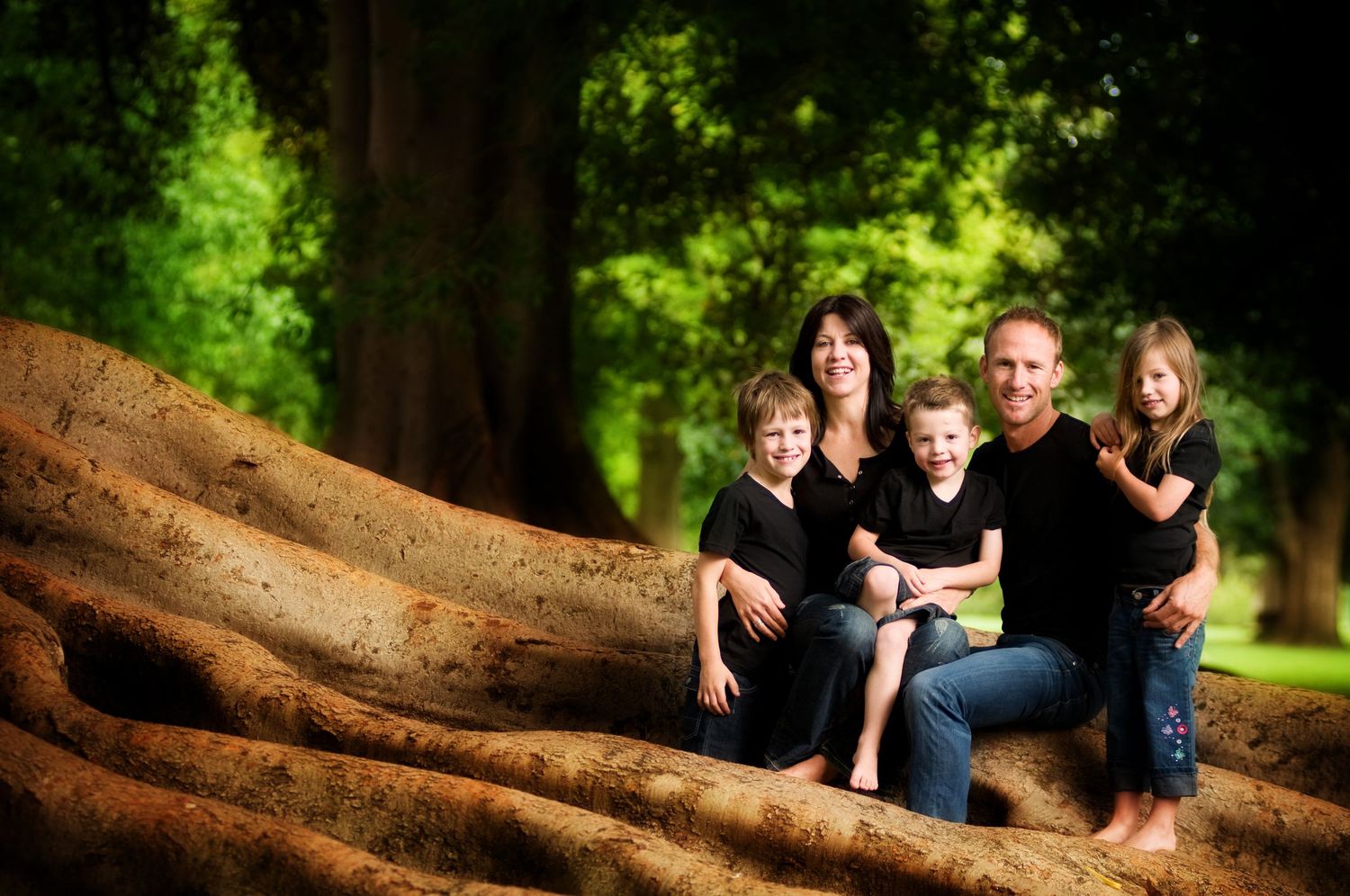 A family photo session showing relaxed poses on a large tree trunk in a lush green forest setting.