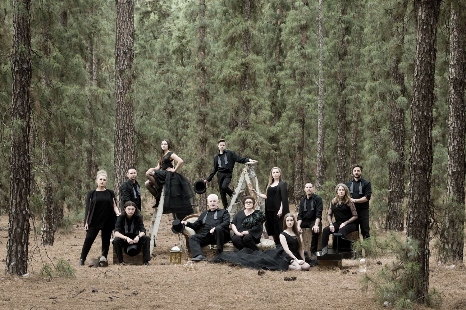 Large group photo session in a pine forest with people sitting on ground.