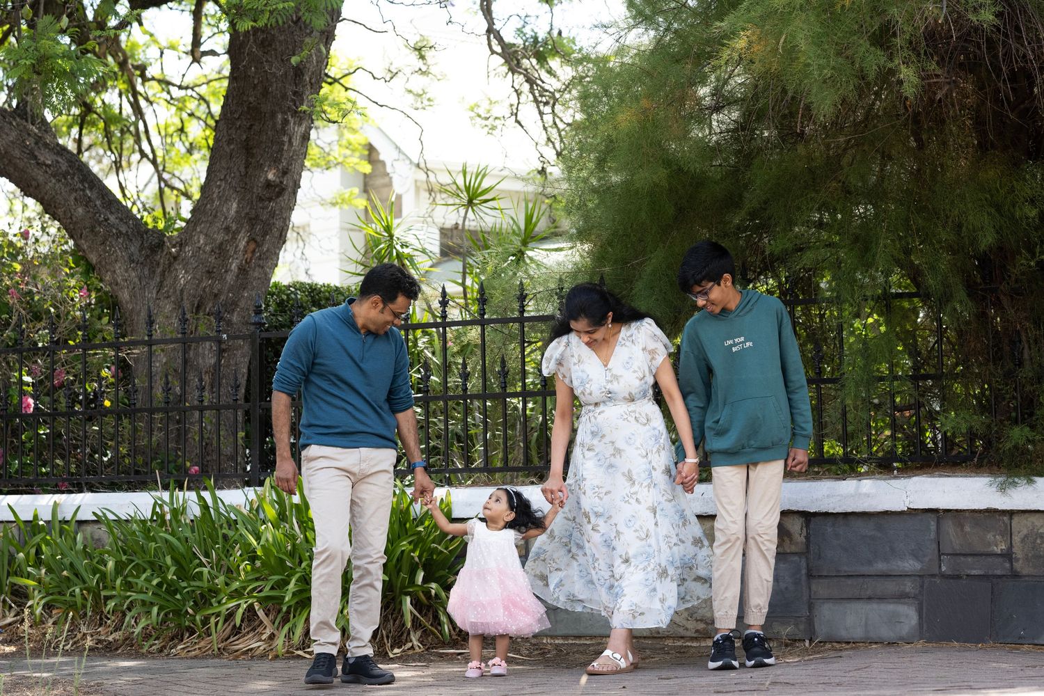 Family walking together along an ornate iron gate and fence in a garden setting.