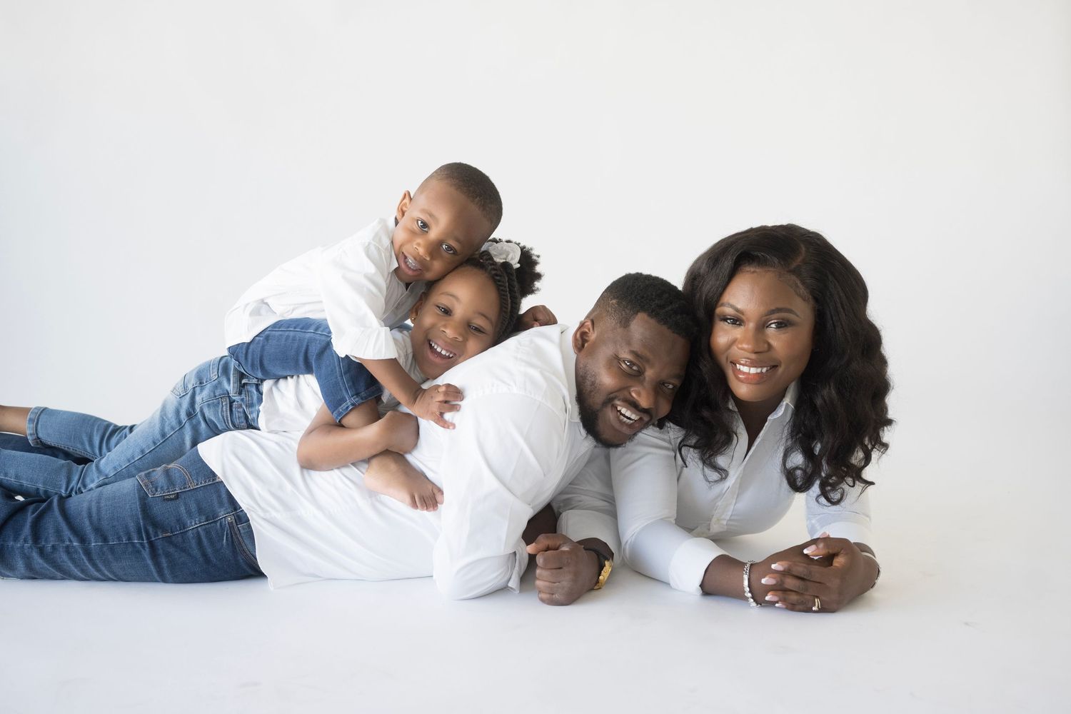 Family lying down together playfully on white studio floor.
