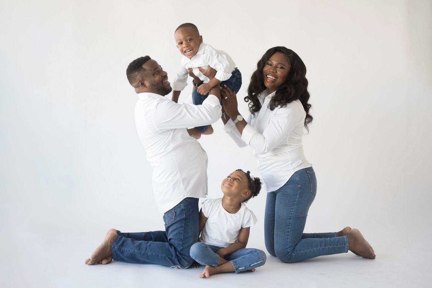 Family posing together on floor in coordinated white and denim outfits.