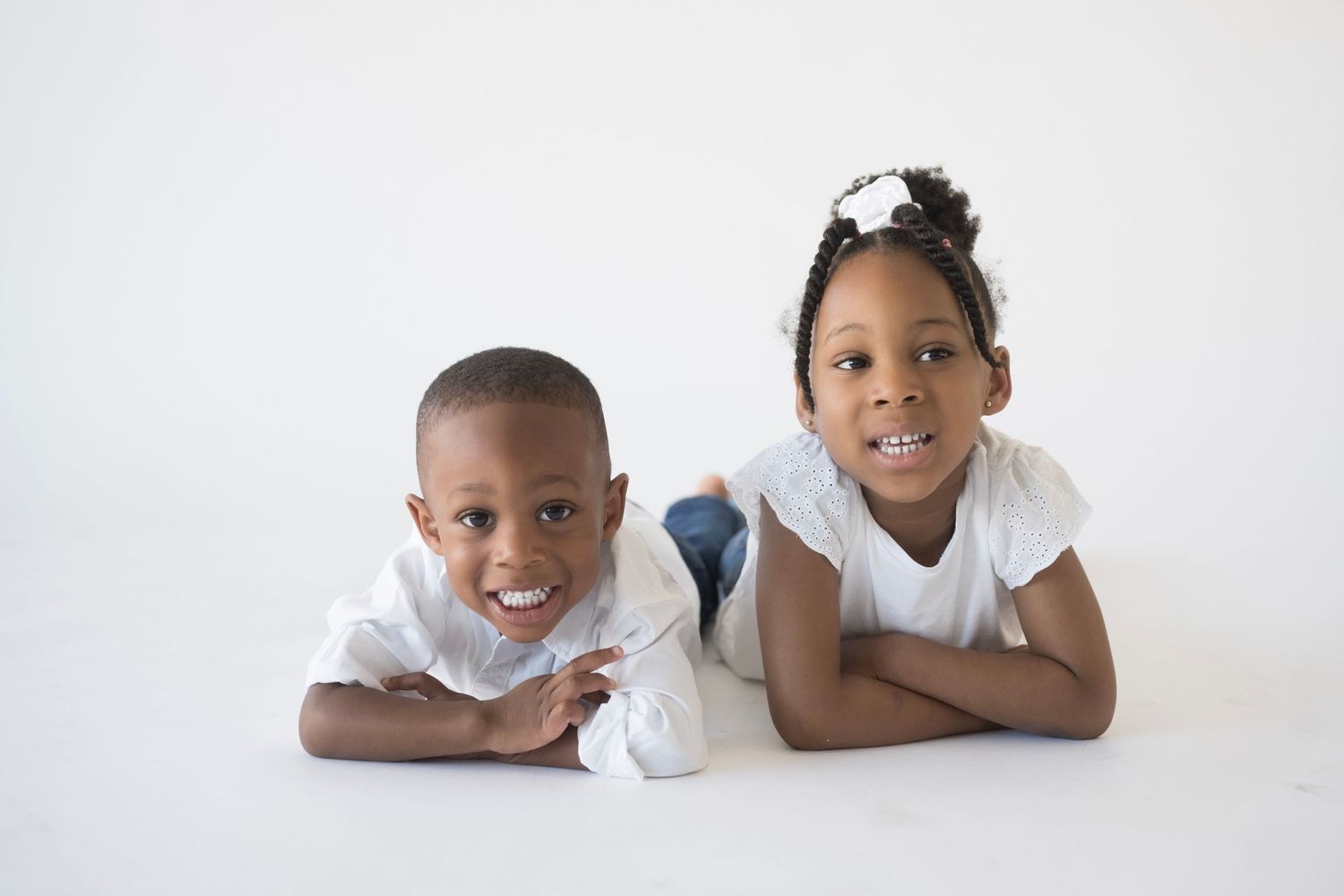 Children lying on white studio floor in casual white outfits.