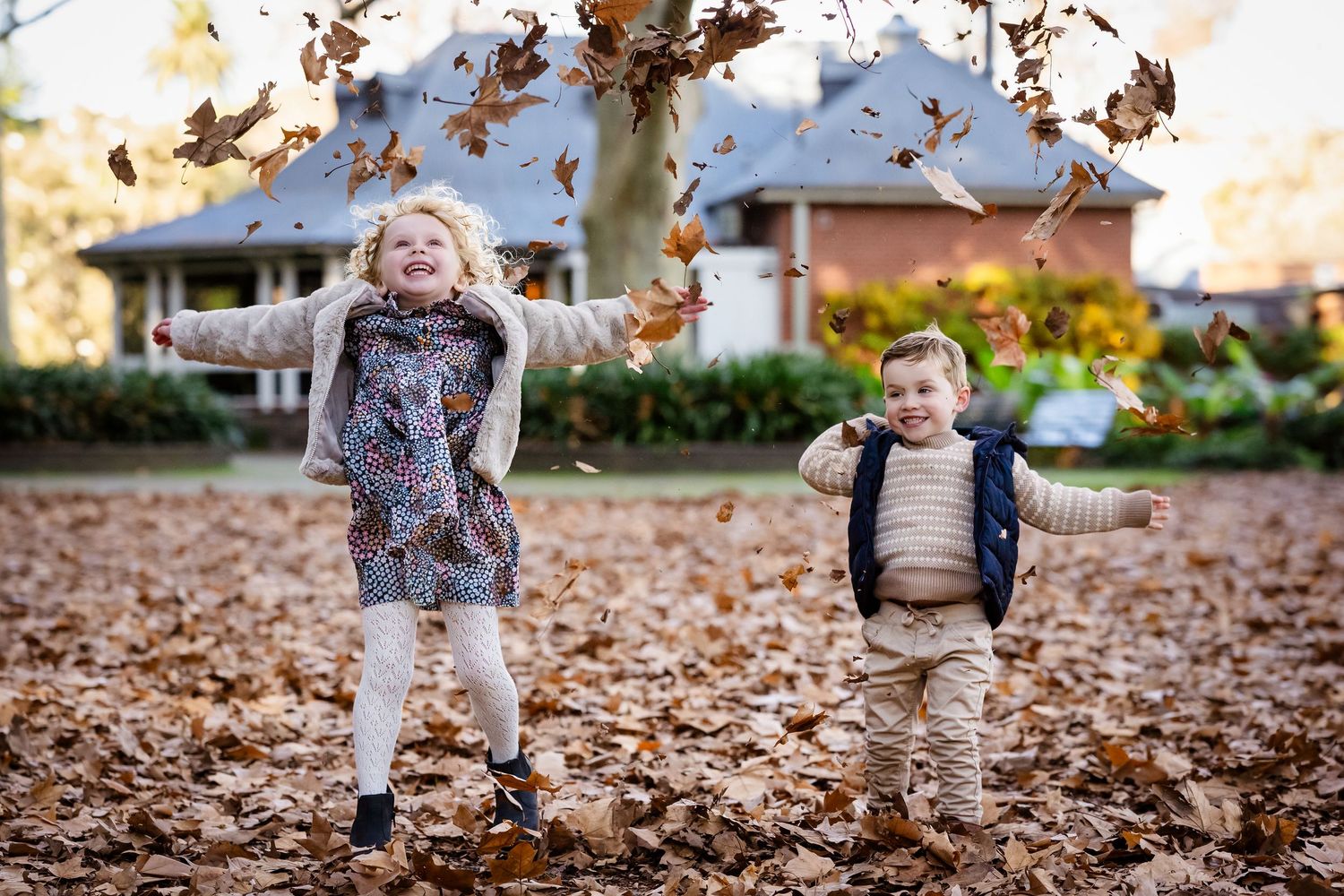 Two young children laughing and tossing autumn leaves in a yard during fall season.