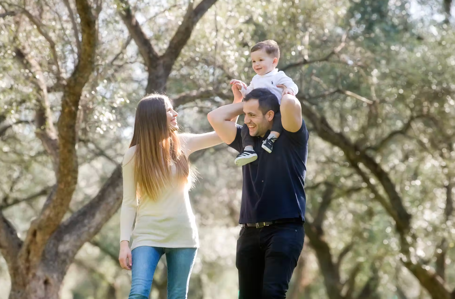 Family photo session outdoors among trees with natural lighting.