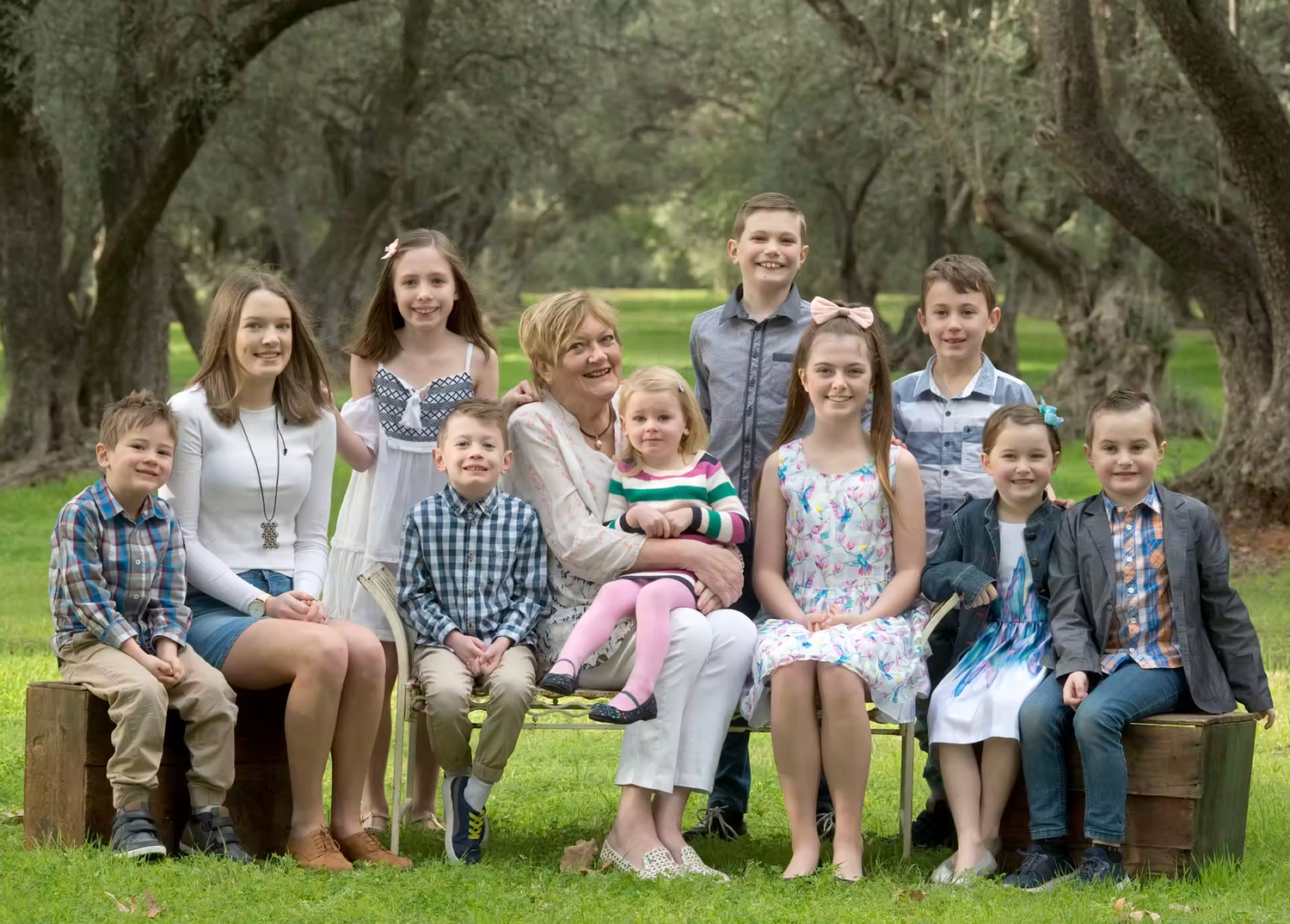 Extended family sitting together outdoors under shady trees for a group photo.