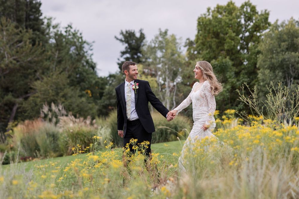 A couple walks together through a scenic meadow filled with vibrant yellow wildflowers on a sunny day.
