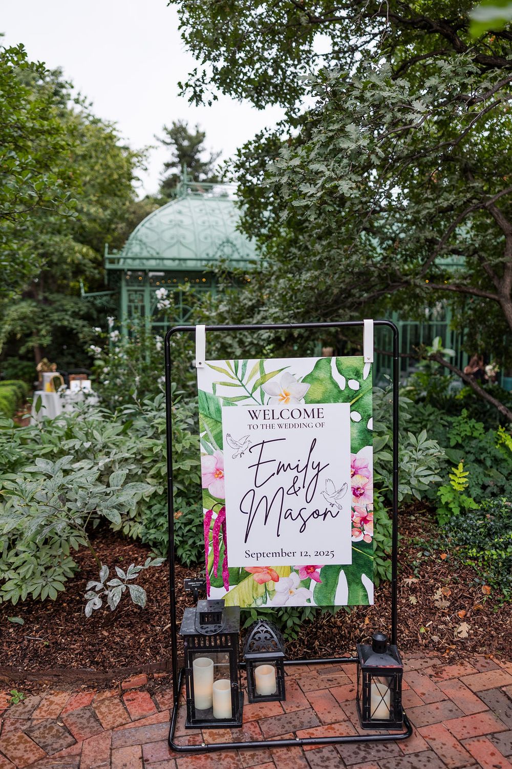 A series of decorative welcome signs and lanterns arranged along a brick pathway in a garden setting.