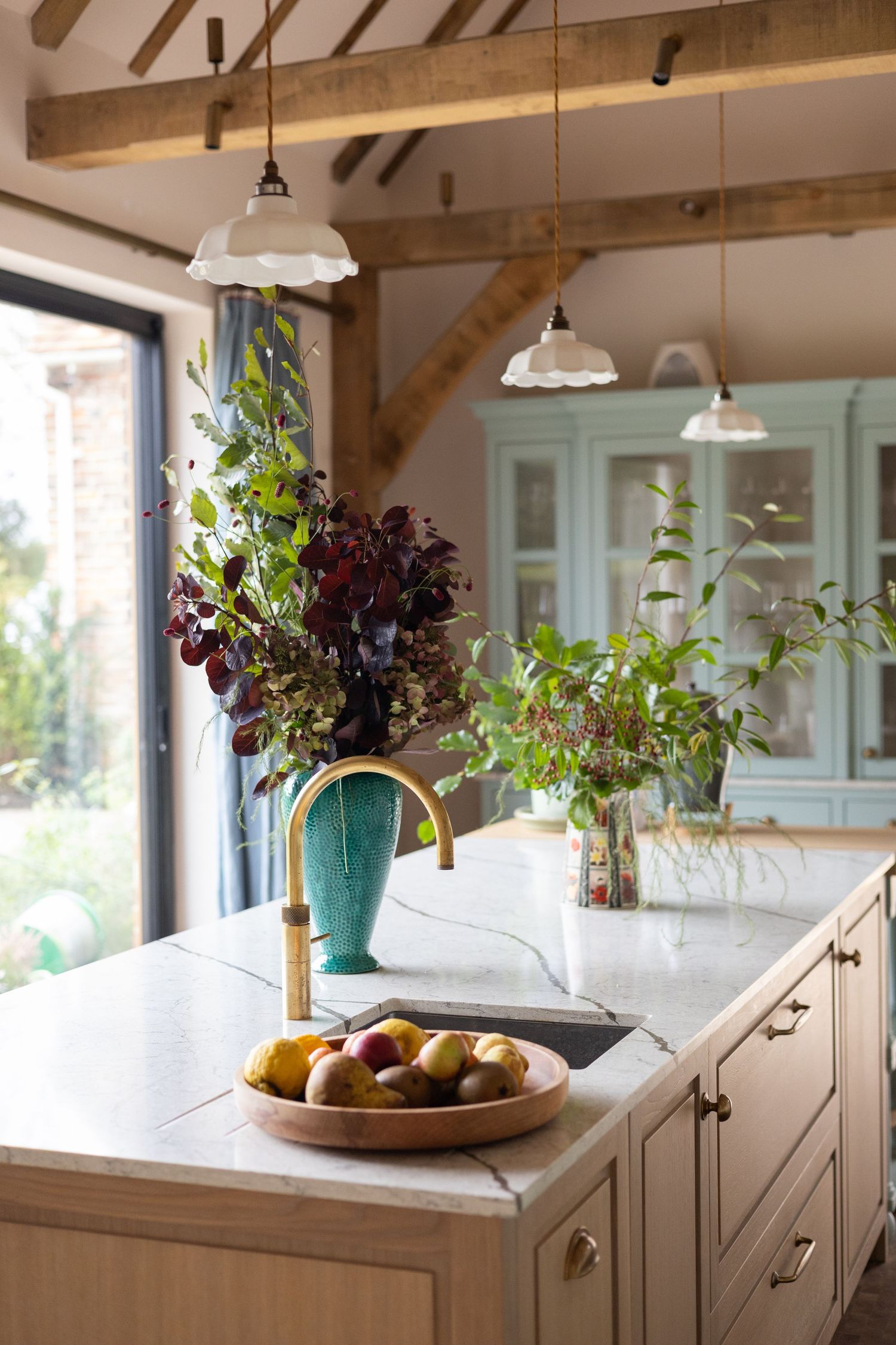 Modern farmhouse kitchen with wood beams, white cabinets, and natural light streaming through windows.