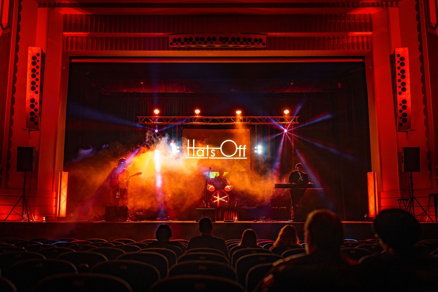 Red illuminated theater interior with rows of empty seats and dramatic stage lighting creates an atmospheric ambiance.