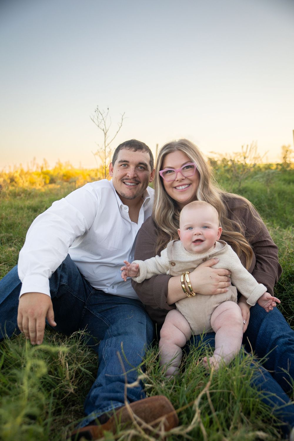 A family sits together in a grassy field during golden hour sunset.