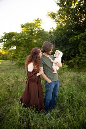 Family stands together in a grassy field at sunset with trees in the background.