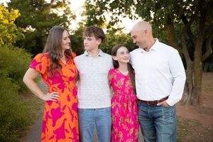 Family members in coordinating pink and orange outfits pose together in a garden setting at sunset.