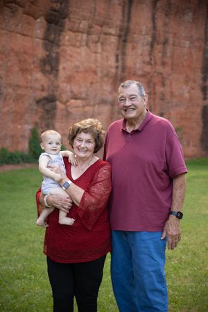 A family of three poses outdoors against a brick wall in coordinating red and blue outfits.