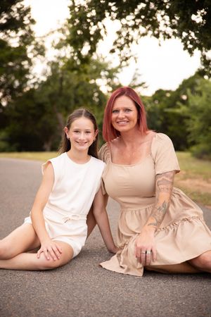 Two people in neutral colored outfits sit together on a paved road during golden hour lighting.