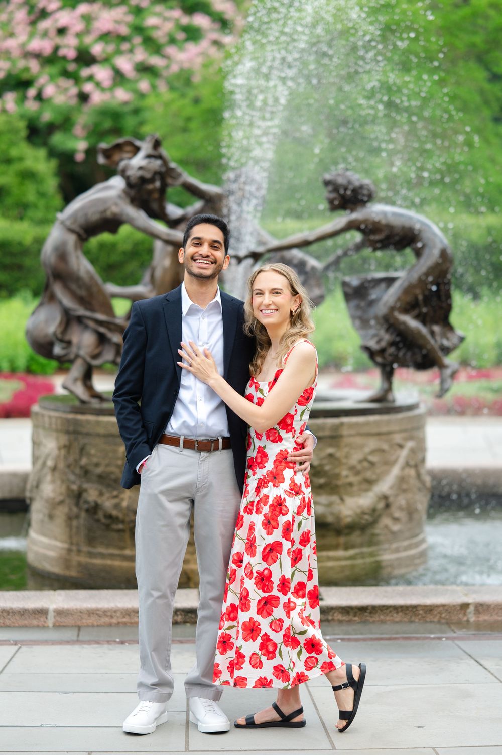 A couple poses playfully by a garden fountain with bronze statues on a spring day.