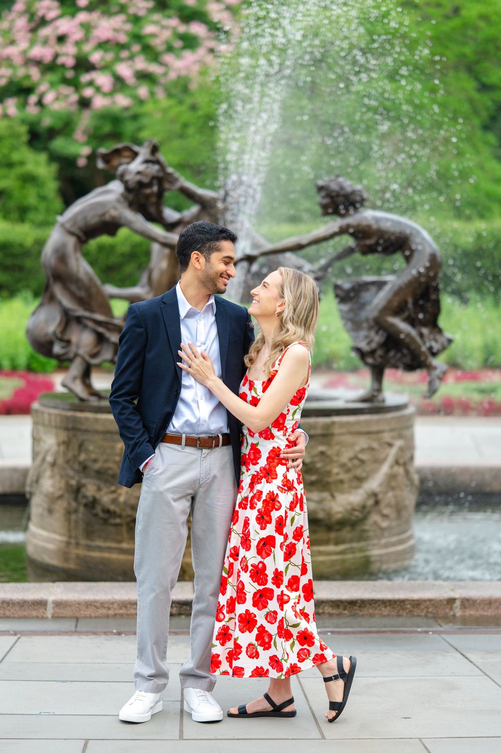 Couple shares romantic moments by a garden fountain with a red and white floral dress and formal attire during their NYC proposal session.