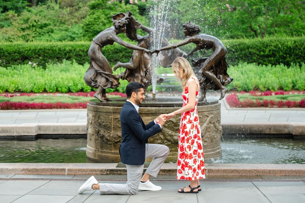 A romantic proposal scene unfolds in the Central Park Conservatory Garden in front of the Untermyer Fountain on a sunny summer day.