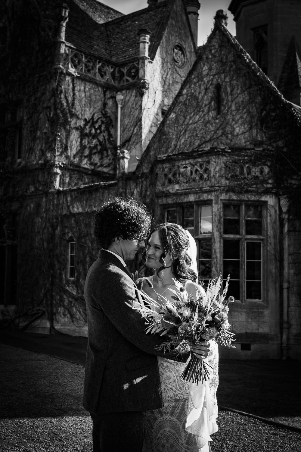 A romantic black and white wedding photo of a couple embracing outside a historic stone building.