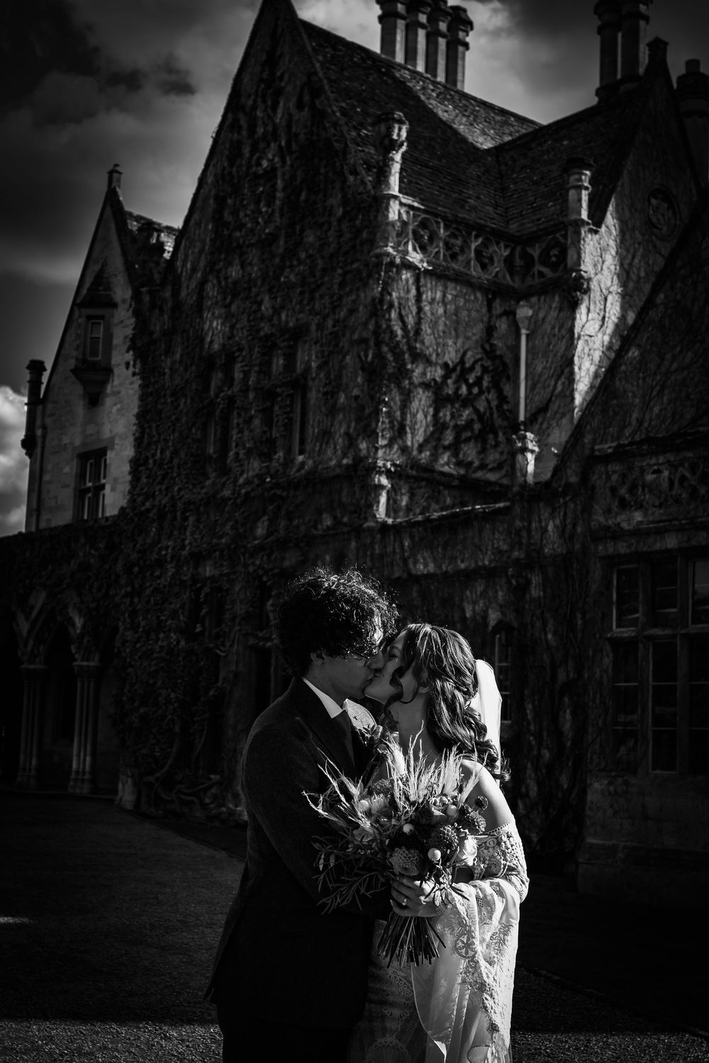 Dramatic black and white wedding portrait against gothic stone building architecture.