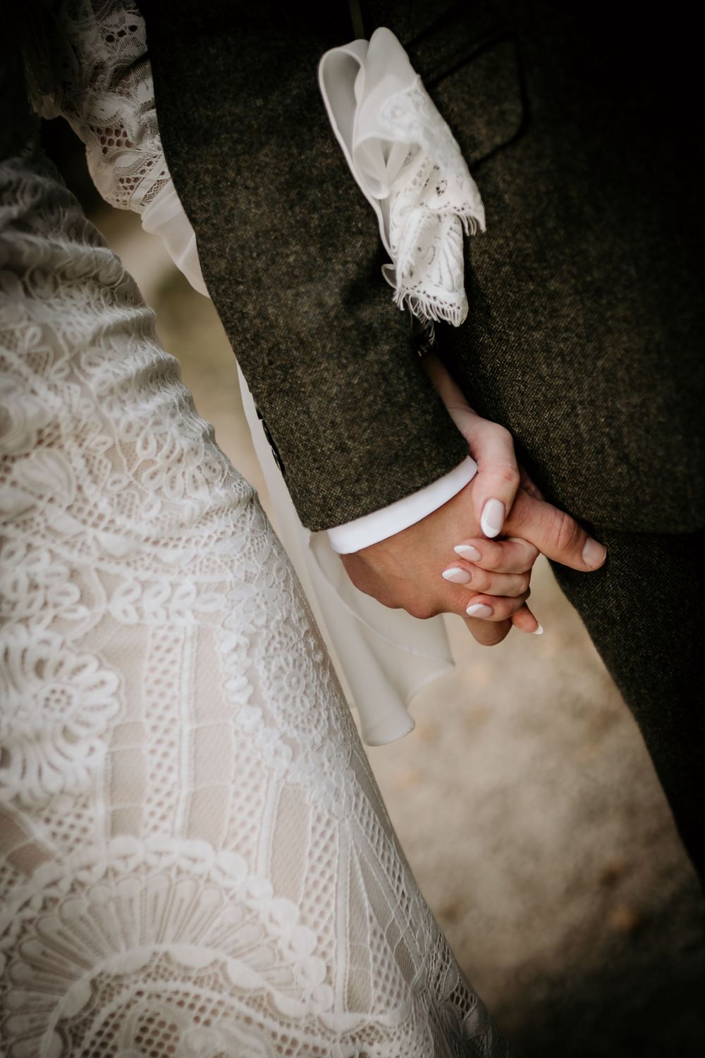 Close-up detail of hands holding against white lace wedding dress fabric.