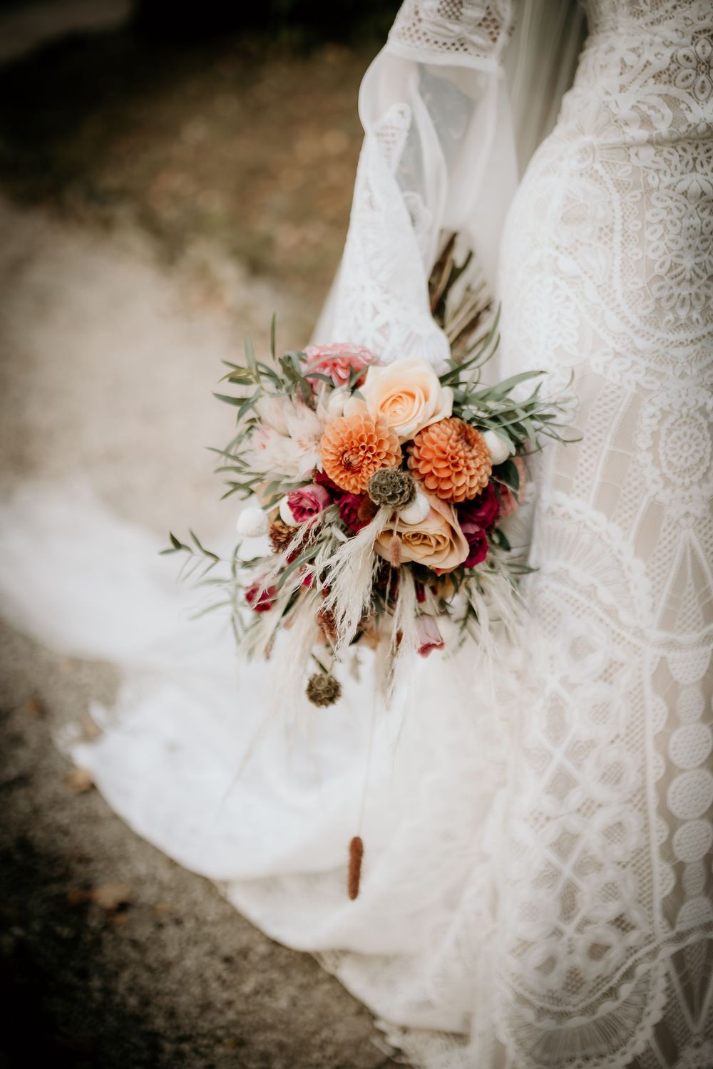Beautiful fall wedding bouquet with peach dahlias and roses against white lace dress in moody lighting.