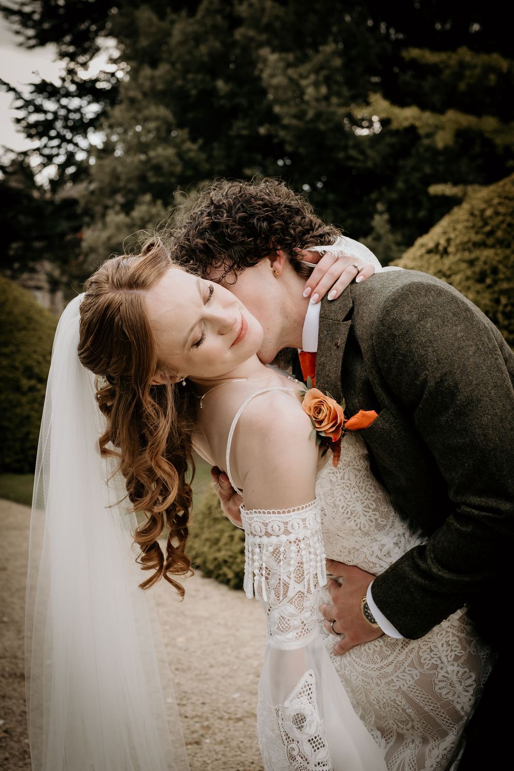 Romantic wedding couple sharing an intimate dip kiss outdoors in a garden setting.