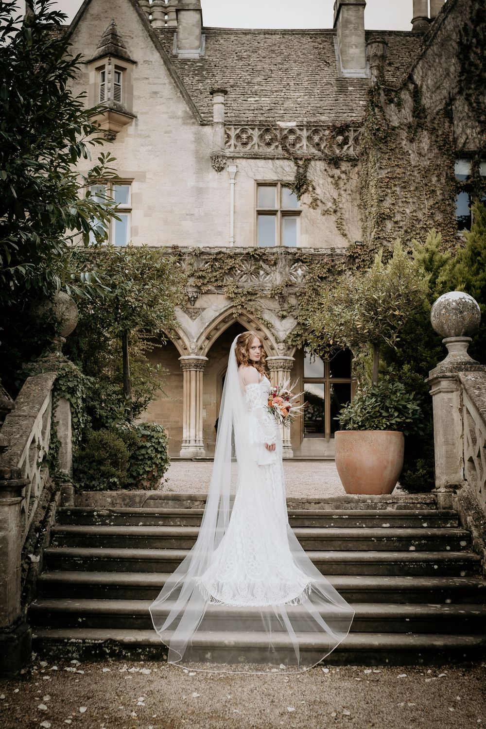 Elegant white wedding dress with flowing veil photographed on stone steps of a historic building.