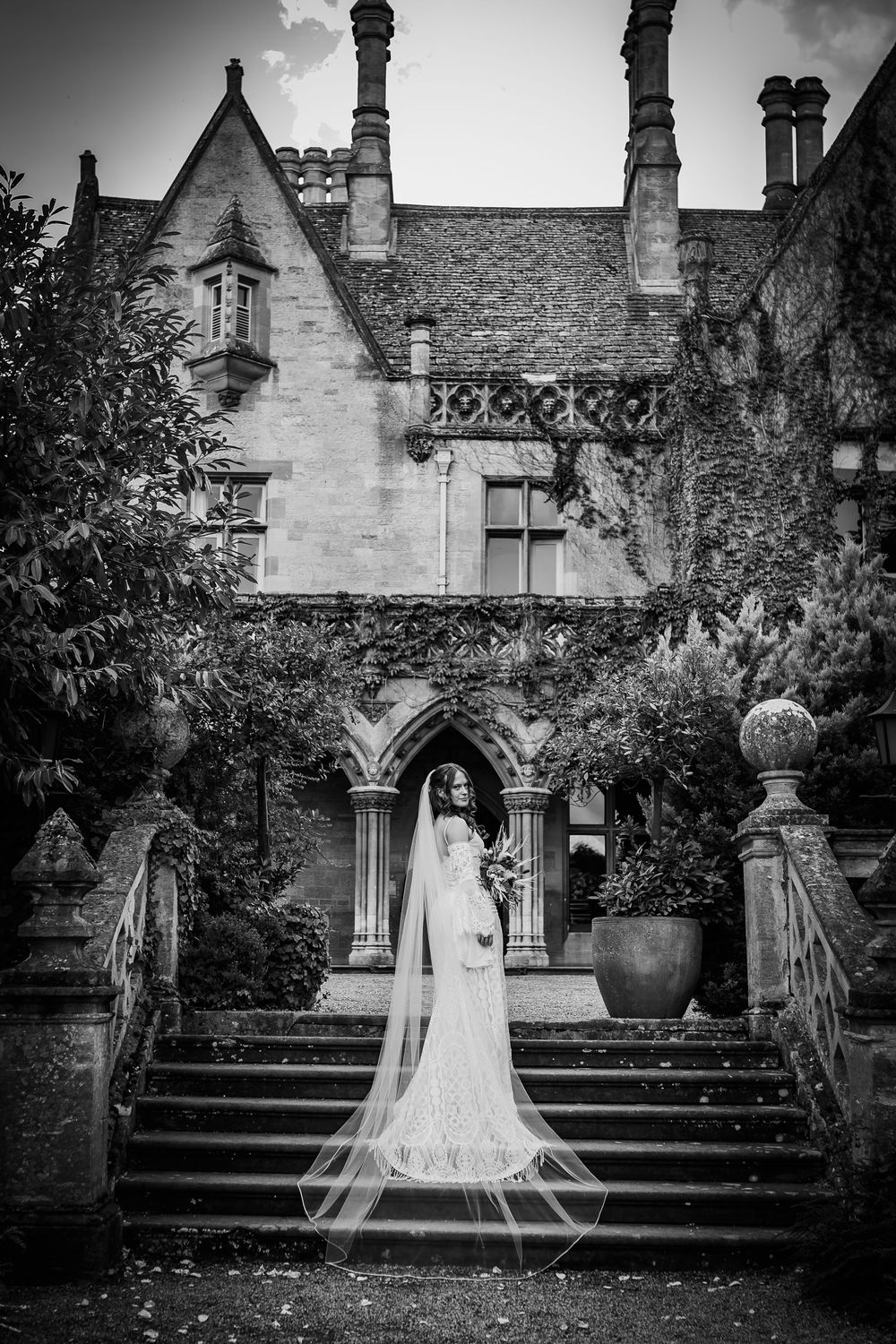 Black and white photo sequence of a bride in a flowing veil standing on stone steps at a Gothic-style mansion.