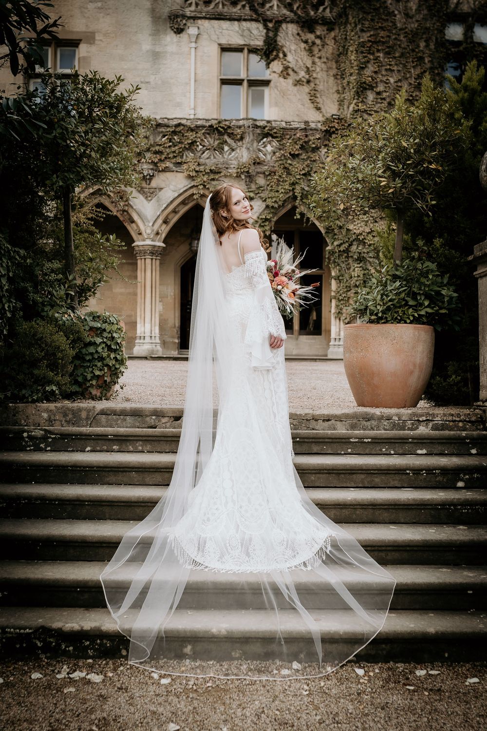 White lace bridal gown with cathedral veil captured on grand stone staircase.
