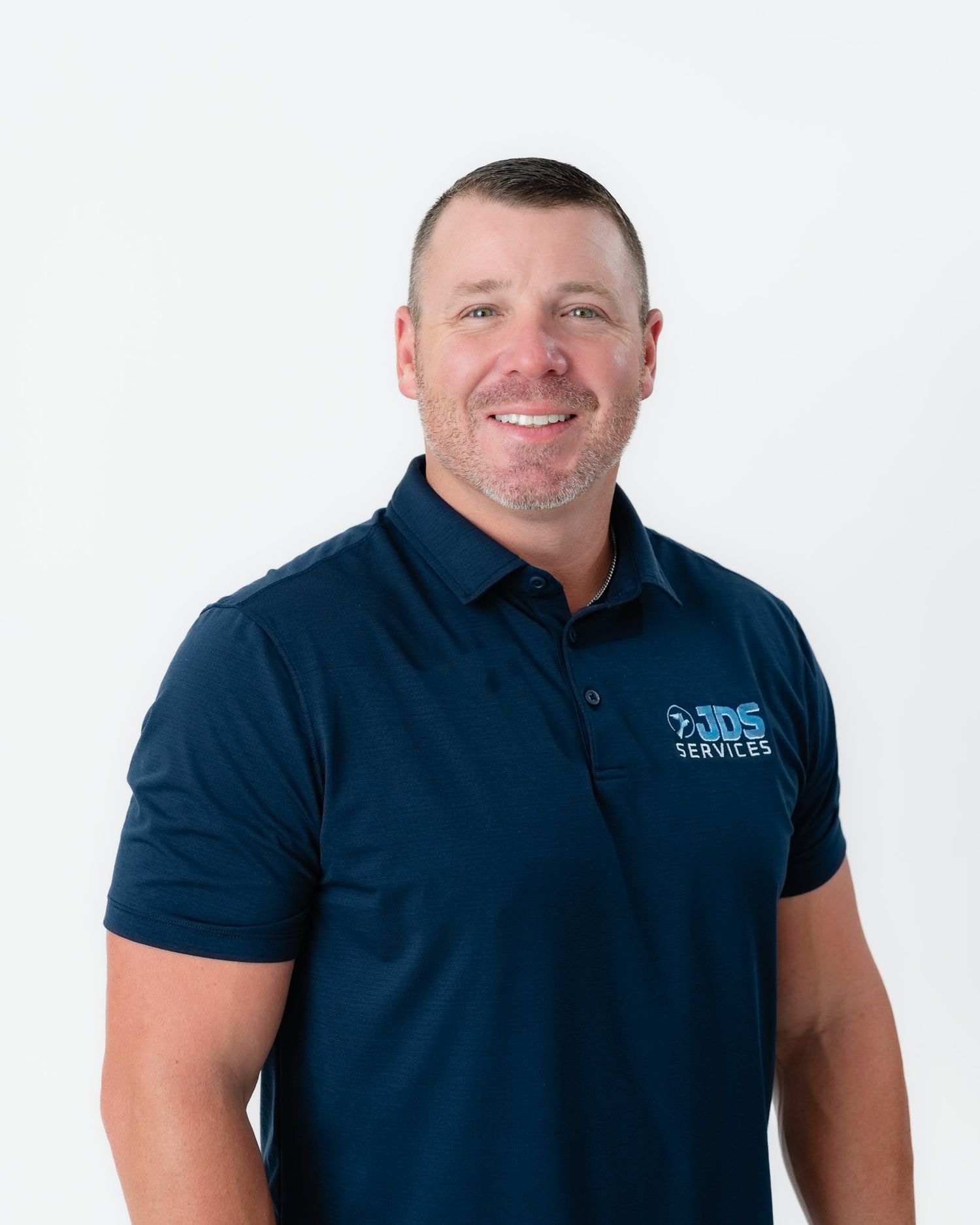 Professional wearing a navy blue polo shirt smiles while posing against a white background.