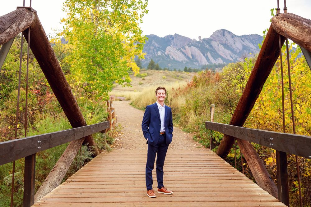 A wooden bridge walkway surrounded by autumn foliage leads to the Flatirons mountains in Boulder, Colorado.