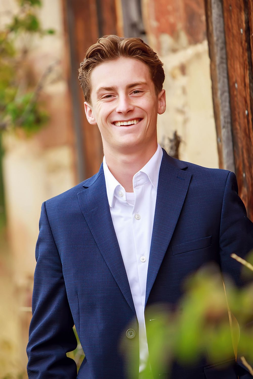Professional portrait in navy suit and white shirt against blurred outdoor background.