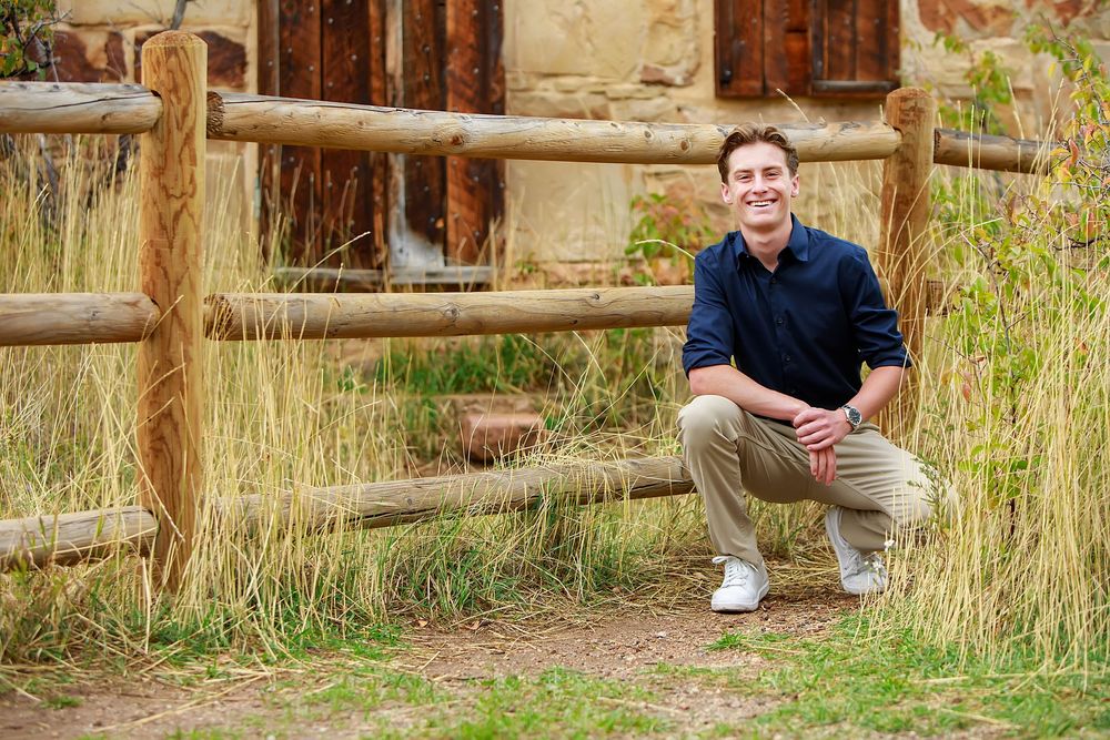 Professional outdoor portrait session with rustic wooden fence and natural grass setting in warm lighting.
