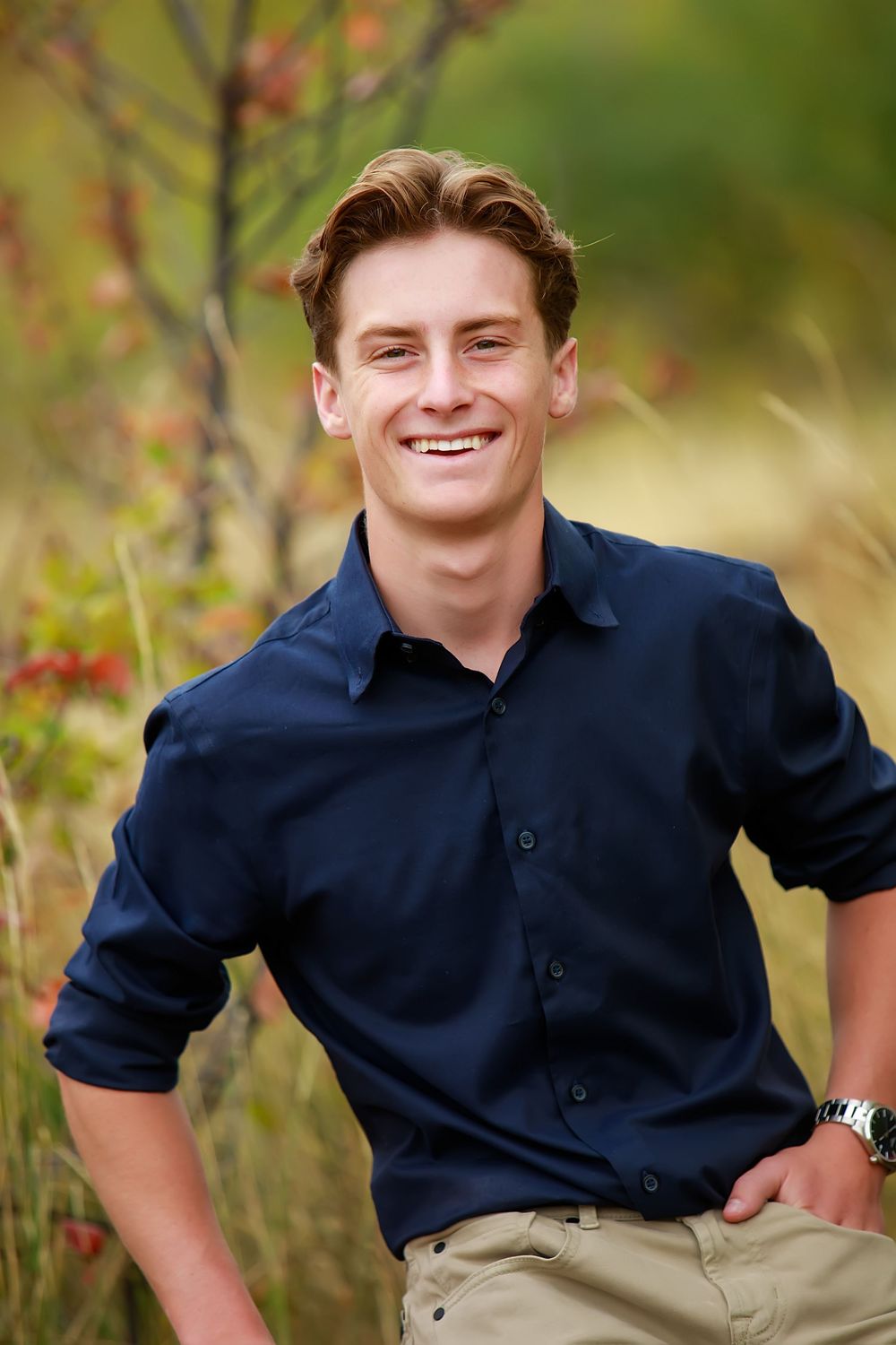 Casual outdoor portrait of someone wearing a dark shirt and khakis with autumn foliage in the background.