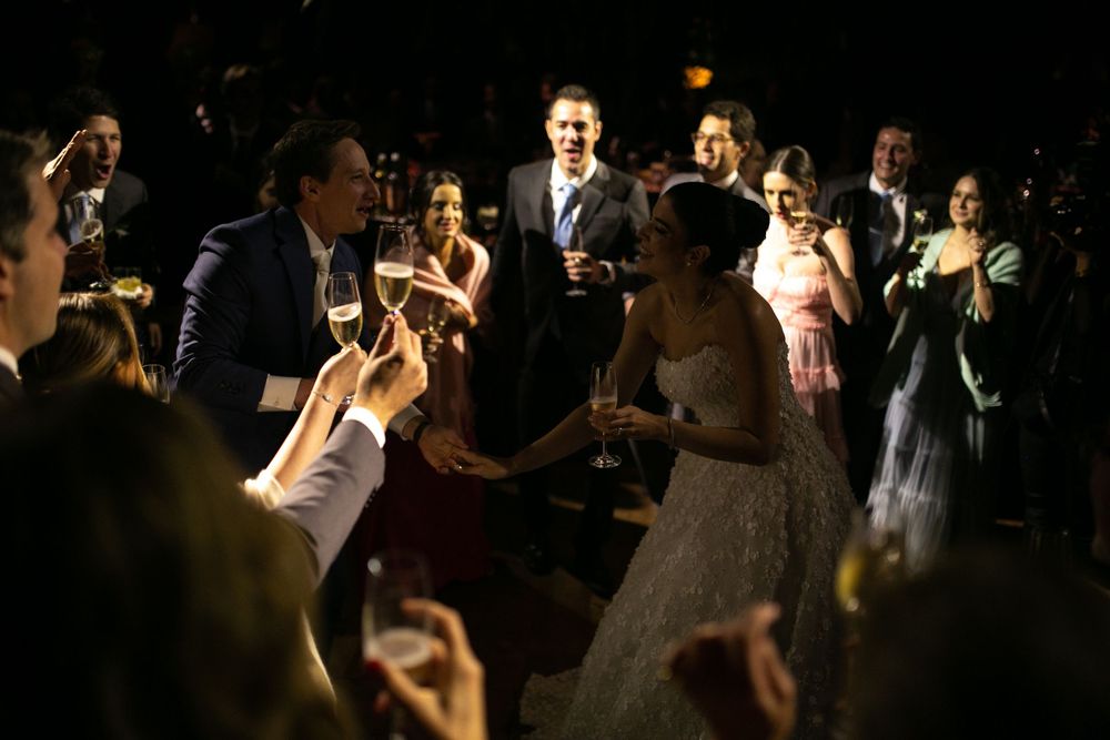 Wedding guests dance together on a dimly lit dance floor during an evening reception celebration.