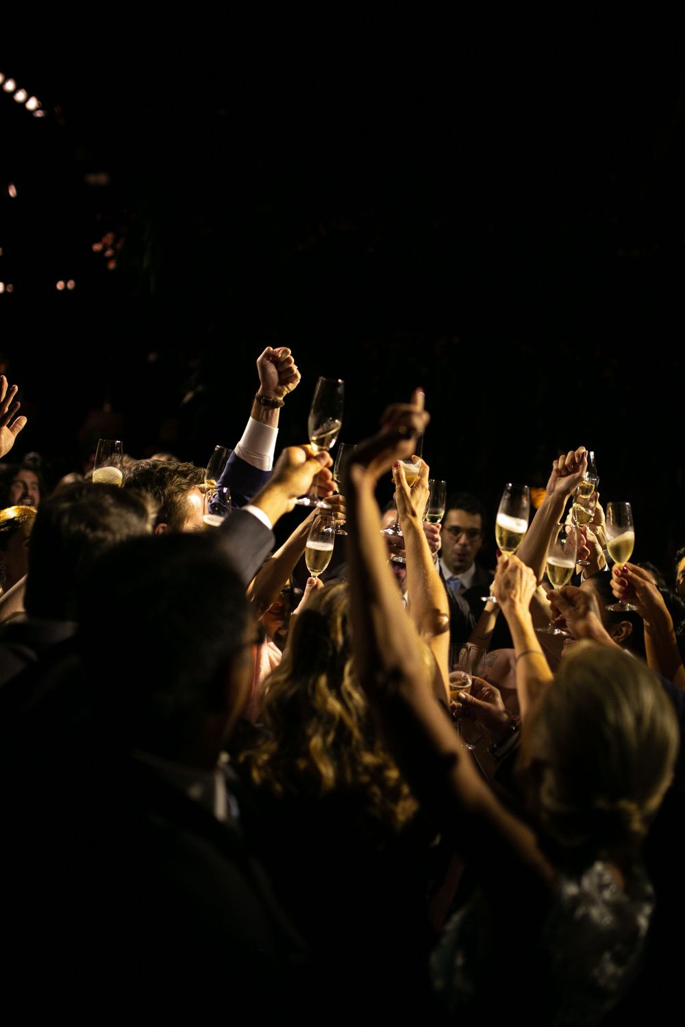 Silhouetted crowd with raised hands at a dark concert or event venue with spotlights in background.