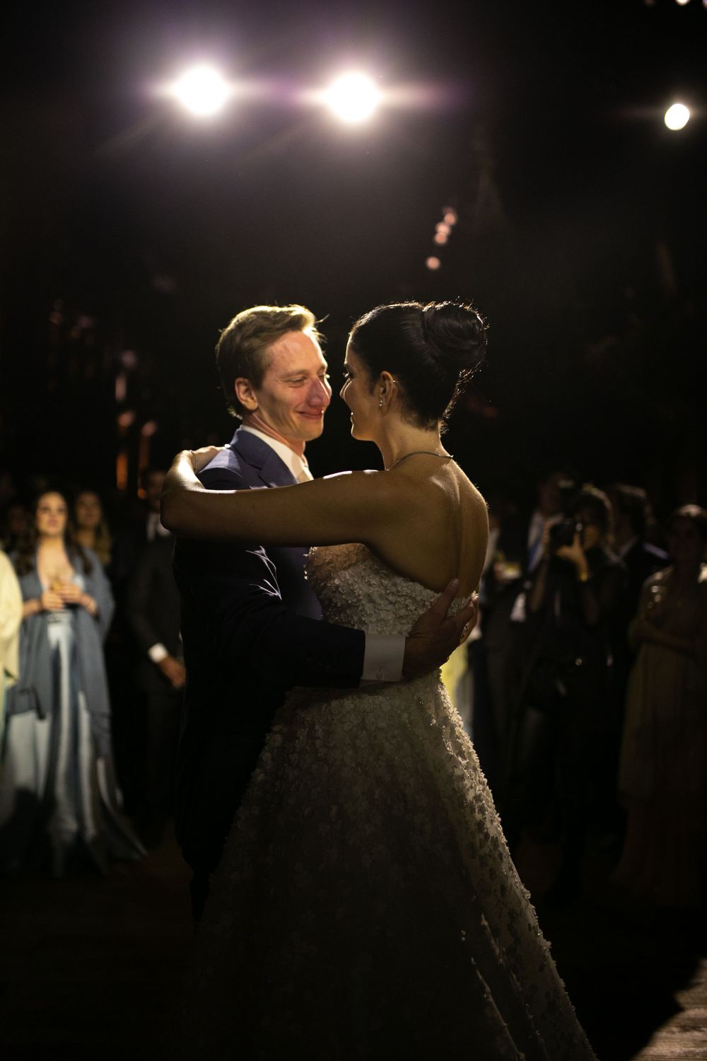 Couple dancing elegantly in formal attire during a wedding reception with dramatic lighting in the background.