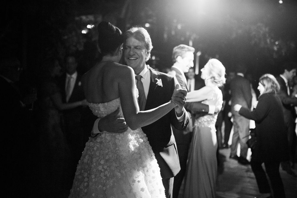 Couples slow dancing together at a dimly lit wedding reception with dramatic backlighting.