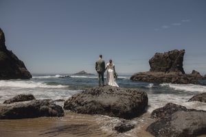 A couple shares a romantic moment on rocky cliffs overlooking dramatic ocean waves at sunset.