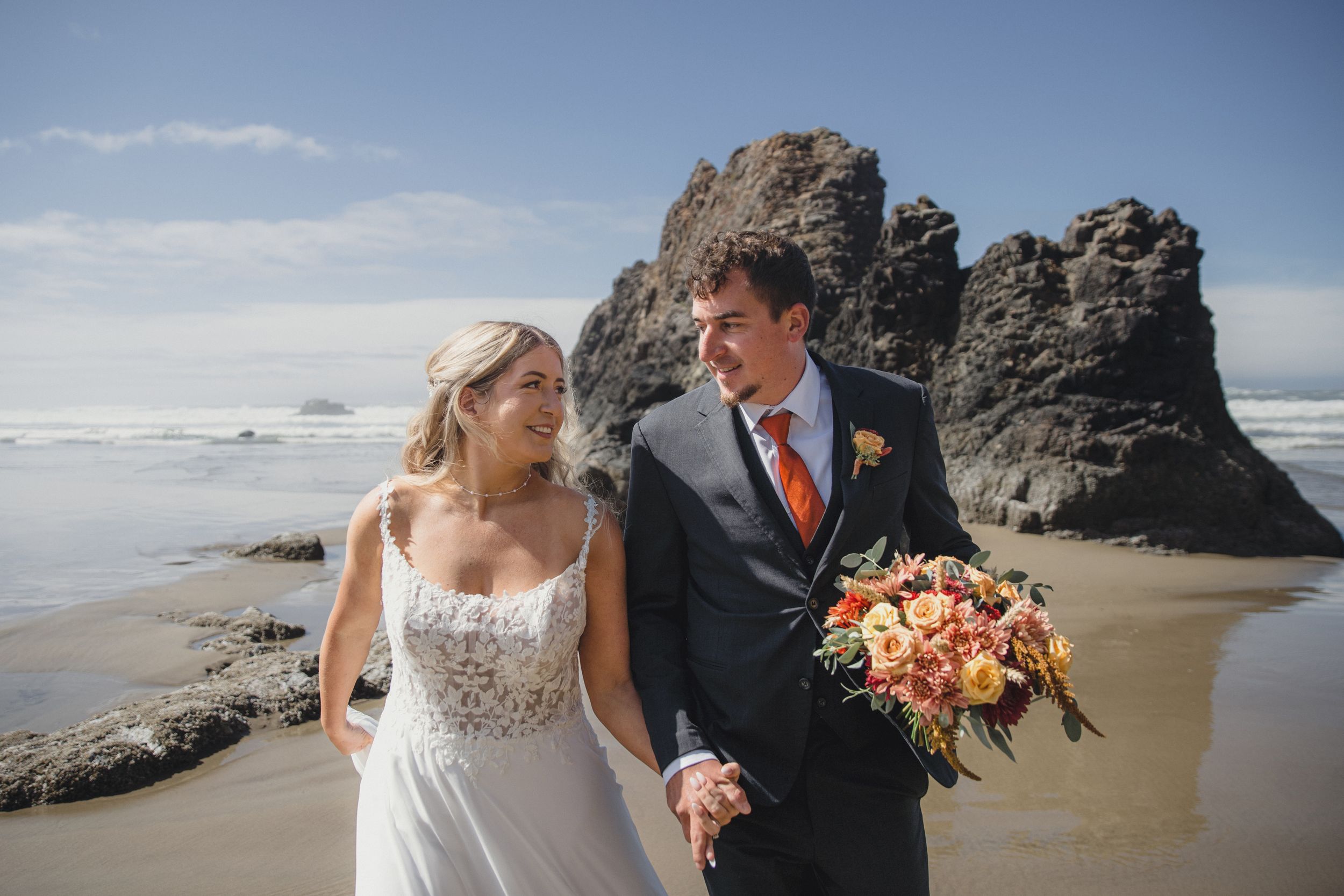 A romantic beach wedding photoshoot with a couple embracing near rocky coastal cliffs and crashing waves.