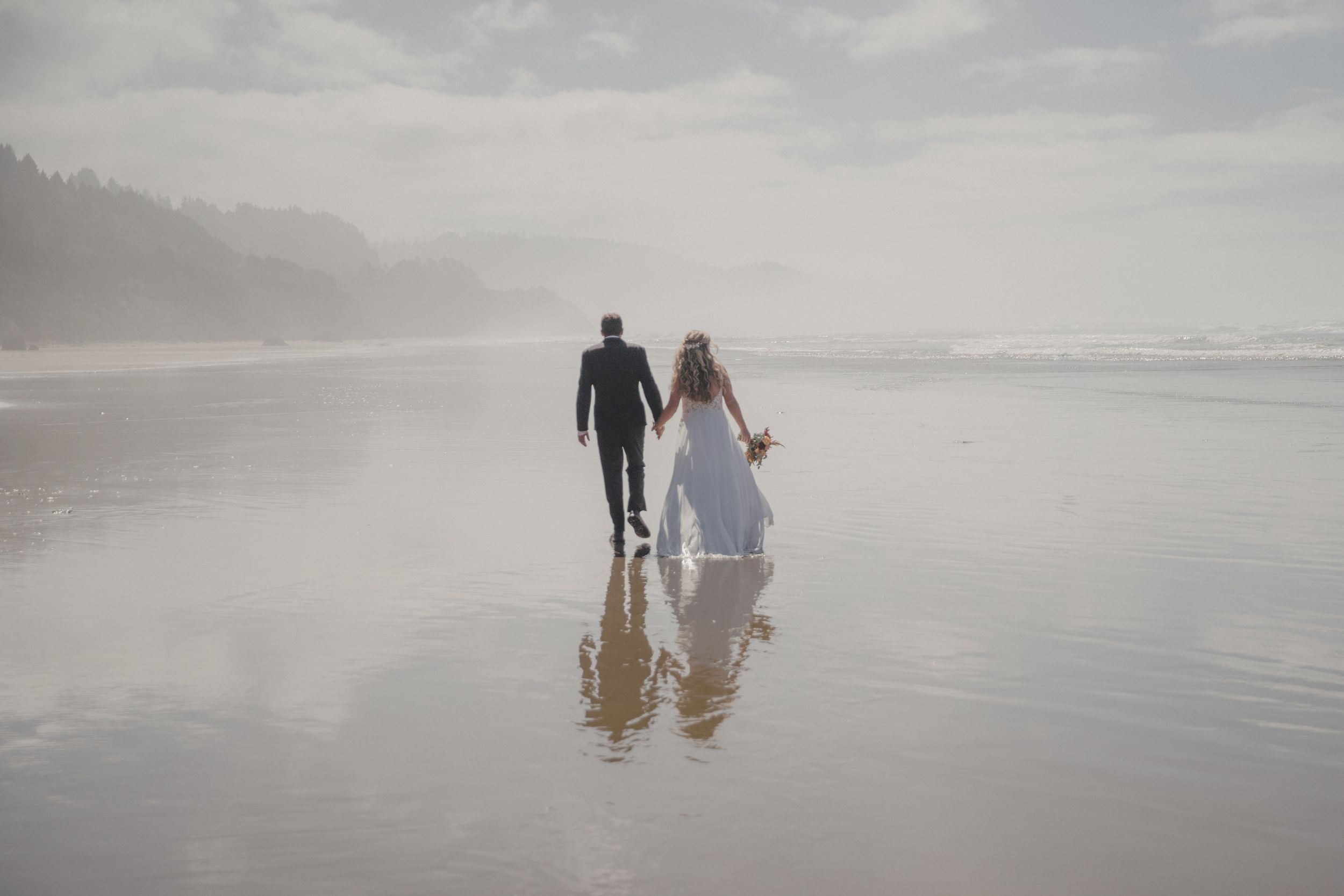 People walking together along a misty beach shore at sunset with waves crashing in the background.