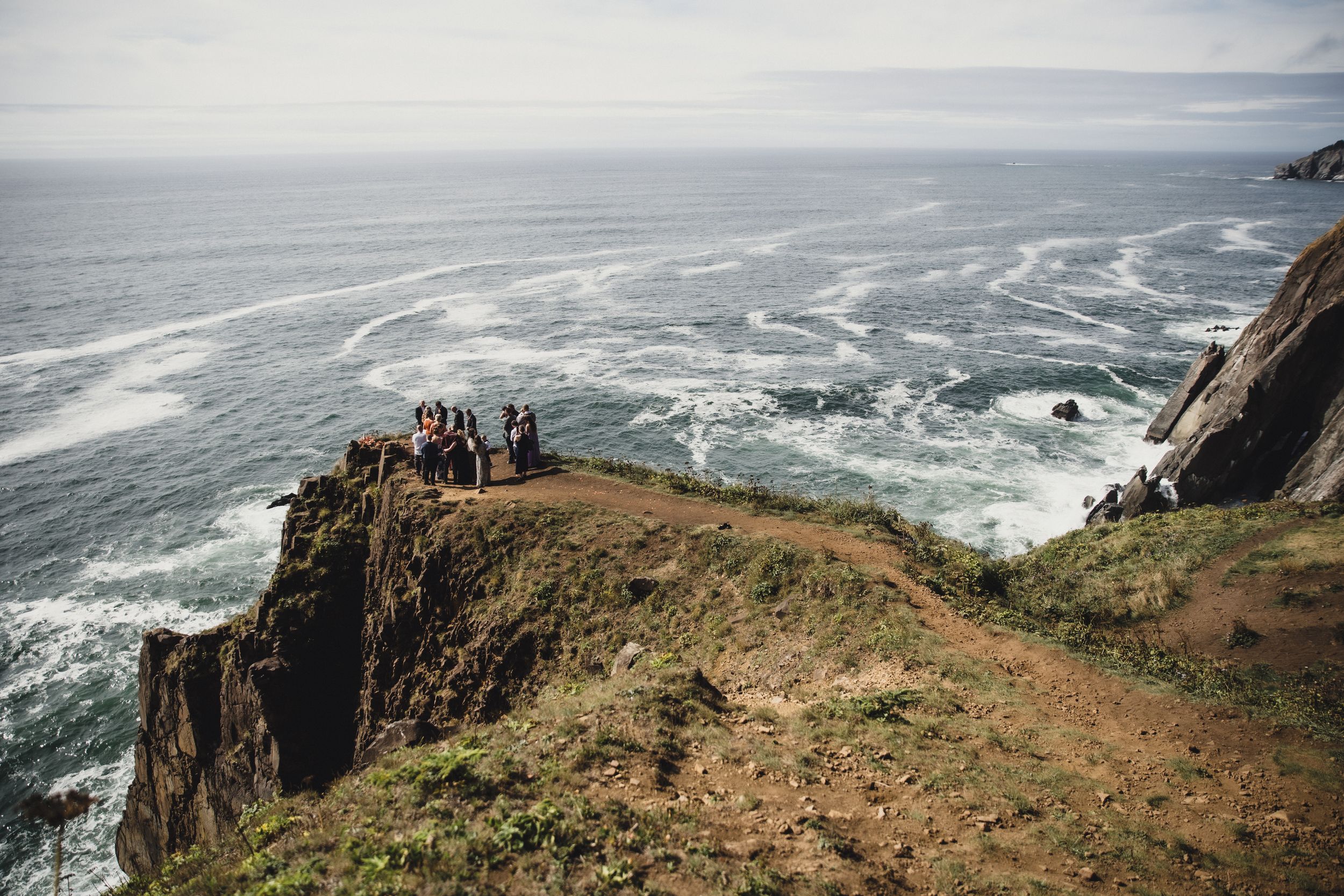 Dramatic coastal cliffs rise above the crashing waves of the Pacific Ocean along a rugged shoreline.