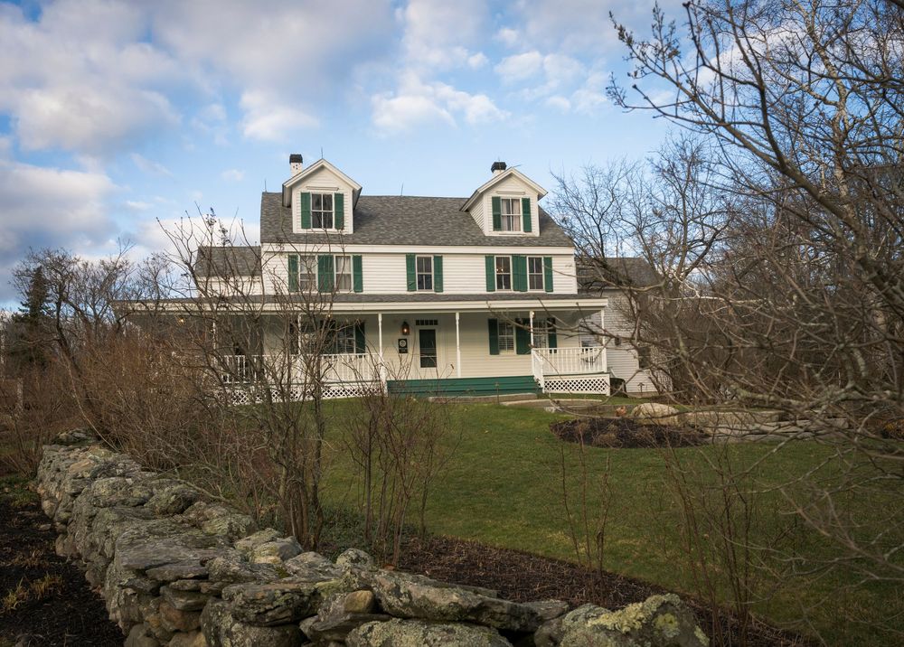 Panoramic view of a colonial-style house on a hilltop with stone walls and bare winter trees in the foreground.