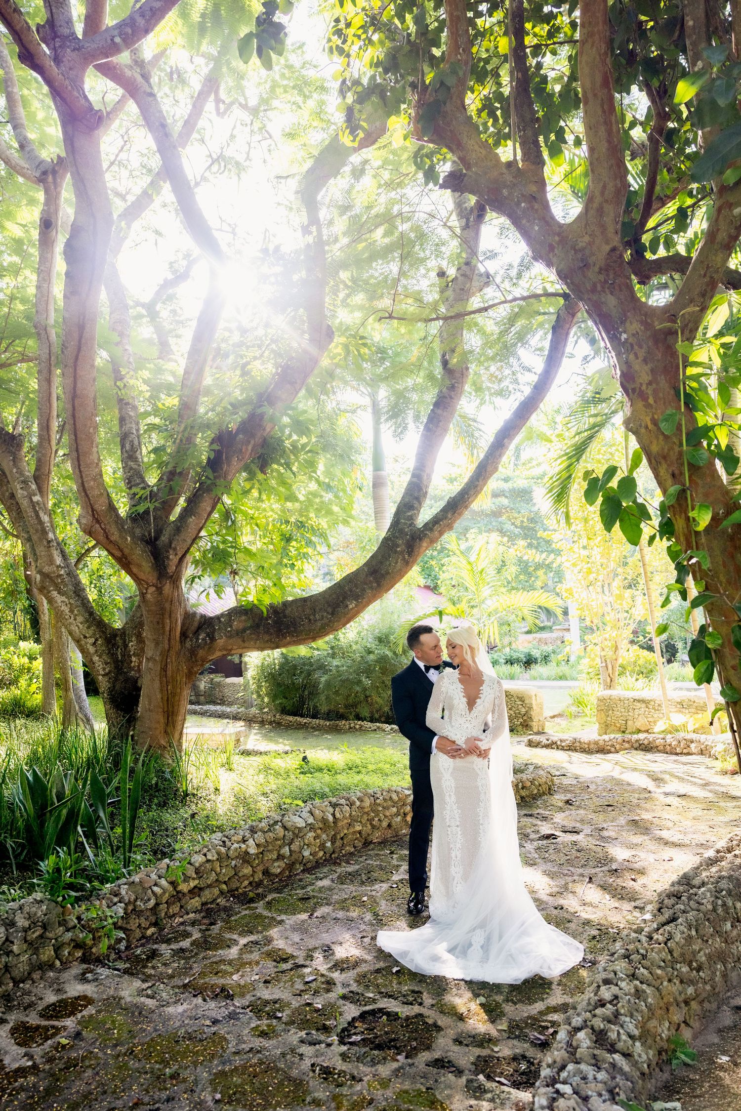 Newlyweds sharing romantic moments in a lush garden setting under green trees. Altos de Chavon