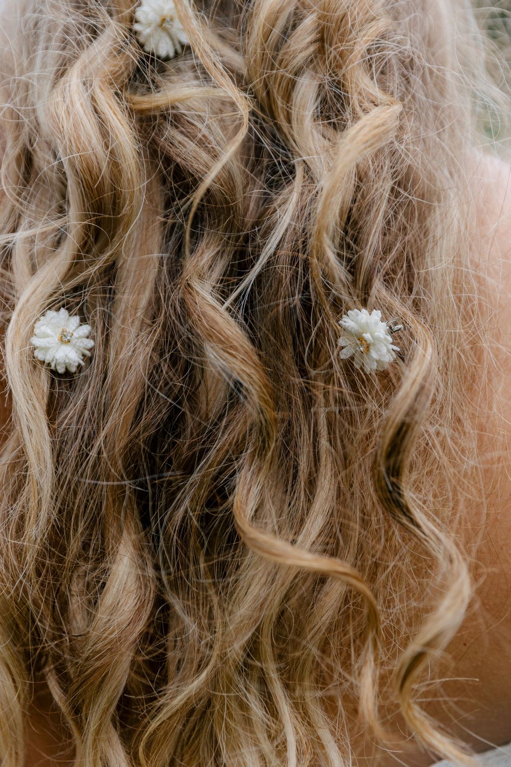 Close-up view of blonde wavy hair adorned with small white floral hair accessories in a romantic bridal style.