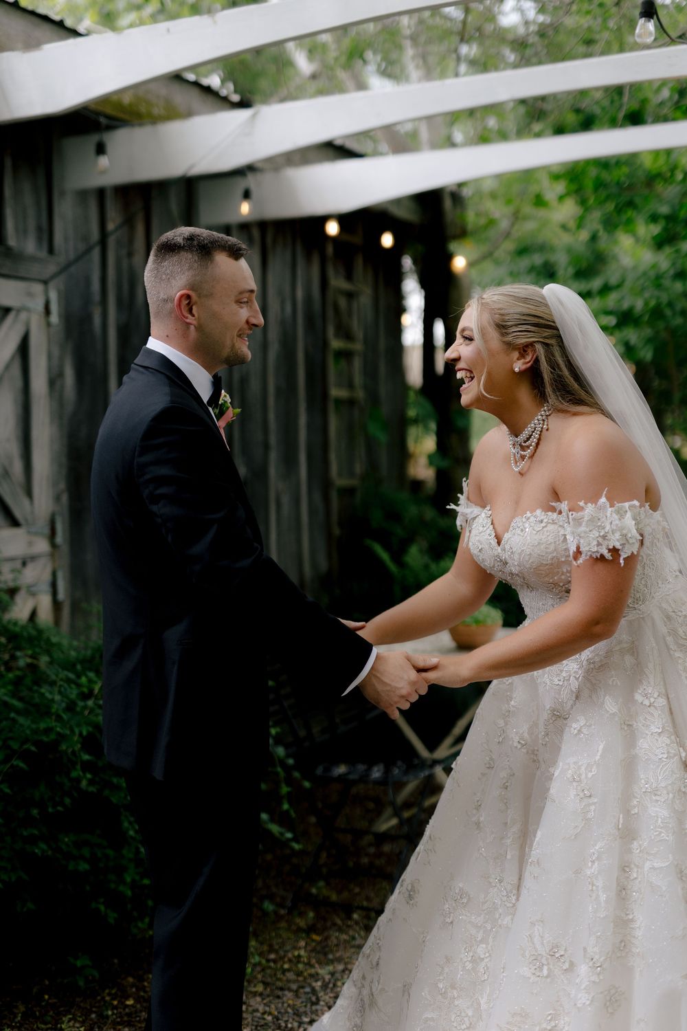A joyful couple shares a candid laughing moment during their outdoor wedding ceremony under string lights.