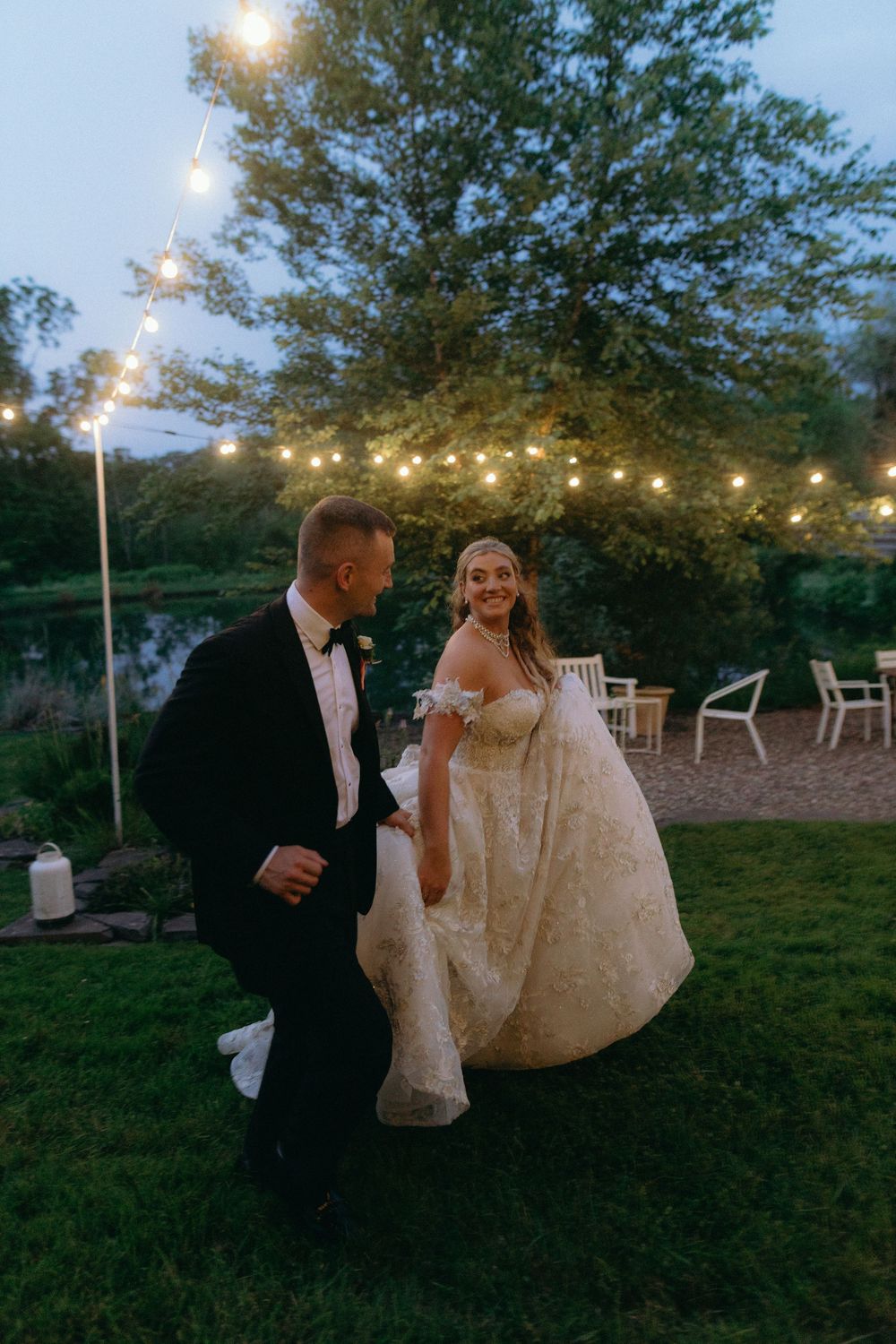 A wedding couple enjoys a magical evening moment under string lights in an outdoor garden setting.