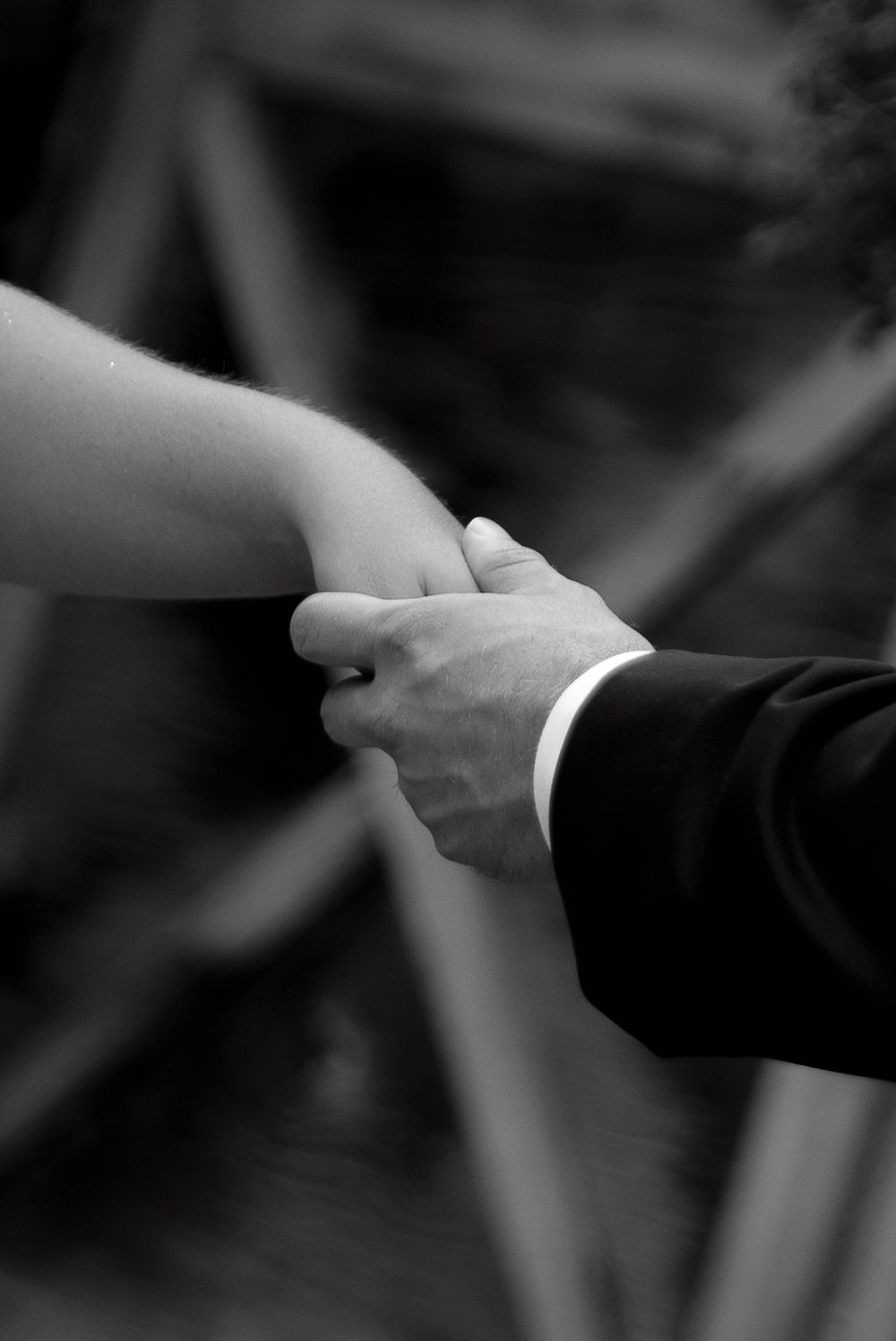 A black and white close-up of hands clasping during a wedding ceremony.