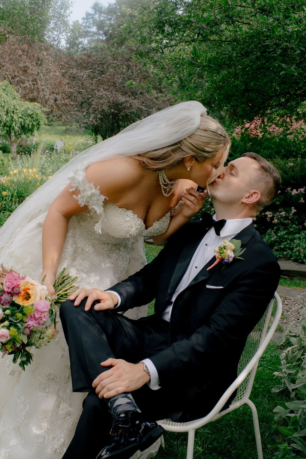 An intimate wedding portrait in a garden setting with vibrant floral bouquet and white chair.